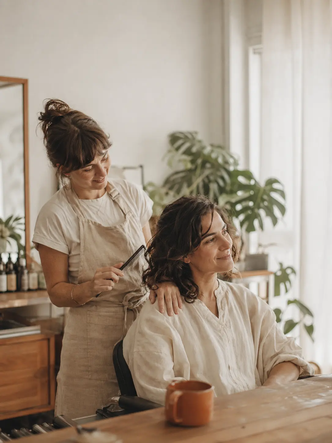 A hairstylist combing a client's hair in a calm, light-filled salon.
